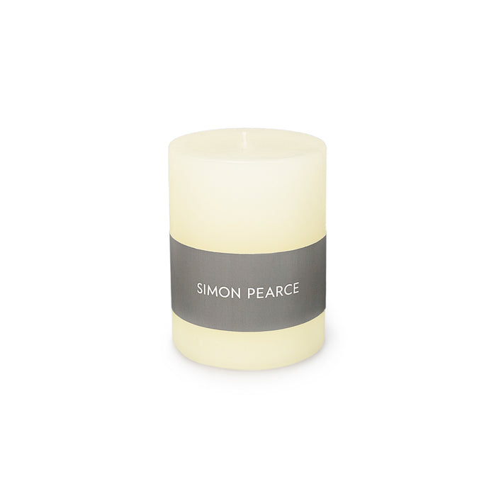 Ivory pillar candle with gray band label reading "SIMON PEARCE" and visible wick at top.