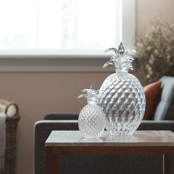 Clear glass pineapple decorative figurines with detailed textured bodies and leaf-shaped tops on a wooden table.
