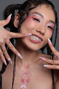 Young woman with pink eye makeup and facial gems smiling to show off sparkling tooth gems and decorated nails.