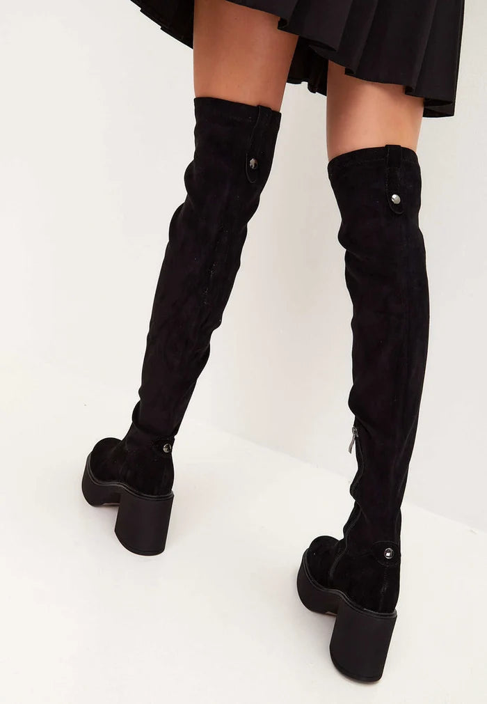 A fashionable woman wearing black suede over-the-knee platform boots, the latest trendy footwear in women's fashion.