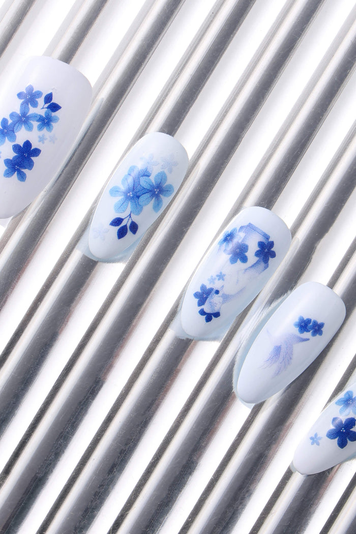 White press-on nails with blue floral designs on silver striped background.