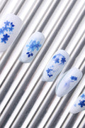 White press-on nails with blue floral designs on silver striped background.