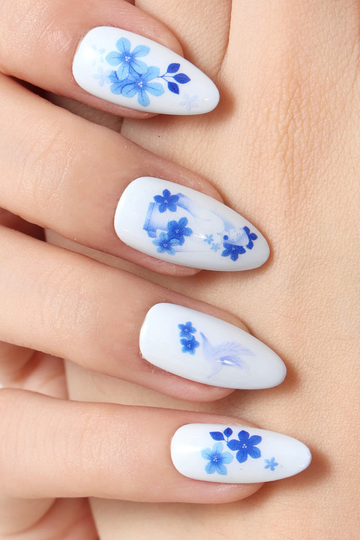 White press-on nails with delicate blue floral designs and a subtle bird motif.