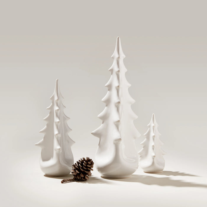 White ceramic evergreen tree figurines in three graduated sizes with a pinecone.