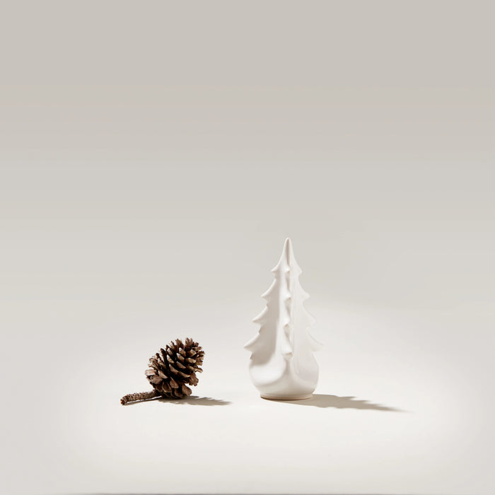 White ceramic evergreen tree-shaped vase with pointed top and tiered silhouette next to a pinecone.