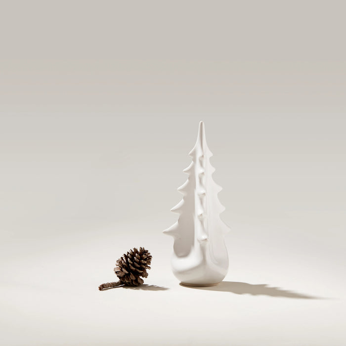 White ceramic evergreen tree-shaped vessel with pointed branches, displayed next to a pinecone.