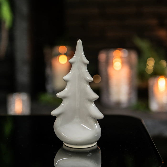 White ceramic evergreen tree figurine with pointed top and tiered branches on rounded base.
