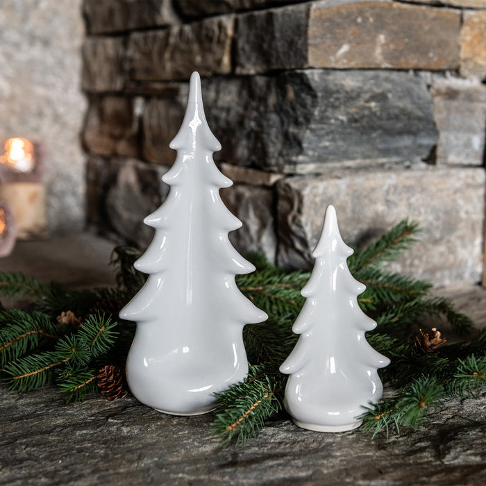 White ceramic evergreen tree figurines in two sizes displayed with green garland and pinecones.