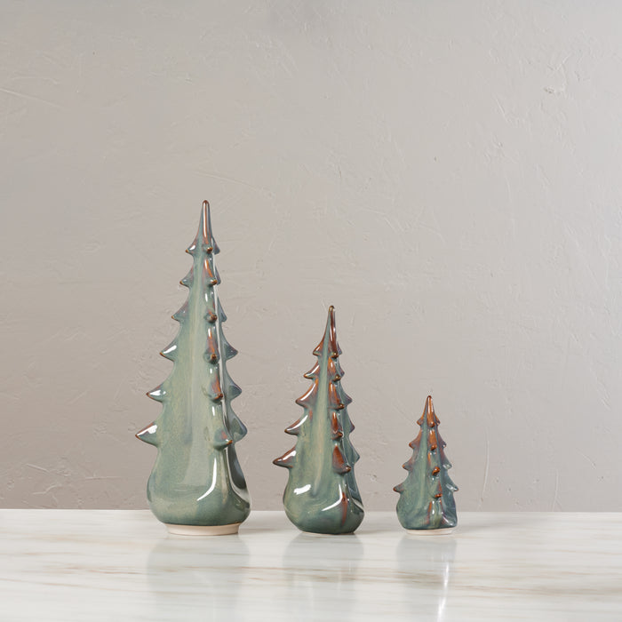 Three ceramic evergreen tree figurines in moss green glaze with metallic accents, arranged by size.