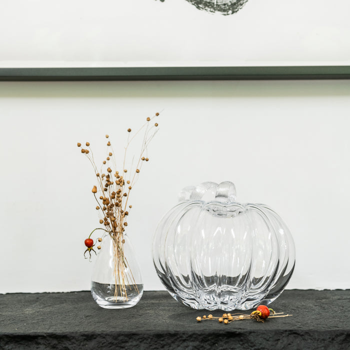 Clear glass pumpkin-shaped decorative object with ribbed texture next to dried berry stems in a small vase.