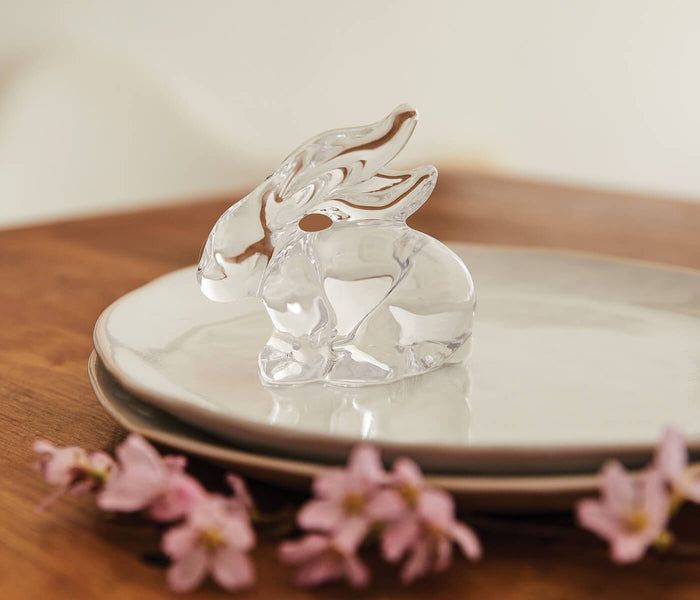 Clear glass rabbit figurine with brown accents sitting on a cream ceramic plate.