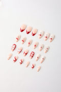 Assorted red and pink press-on nails with cherry, bow, stripe, and rhinestone designs.