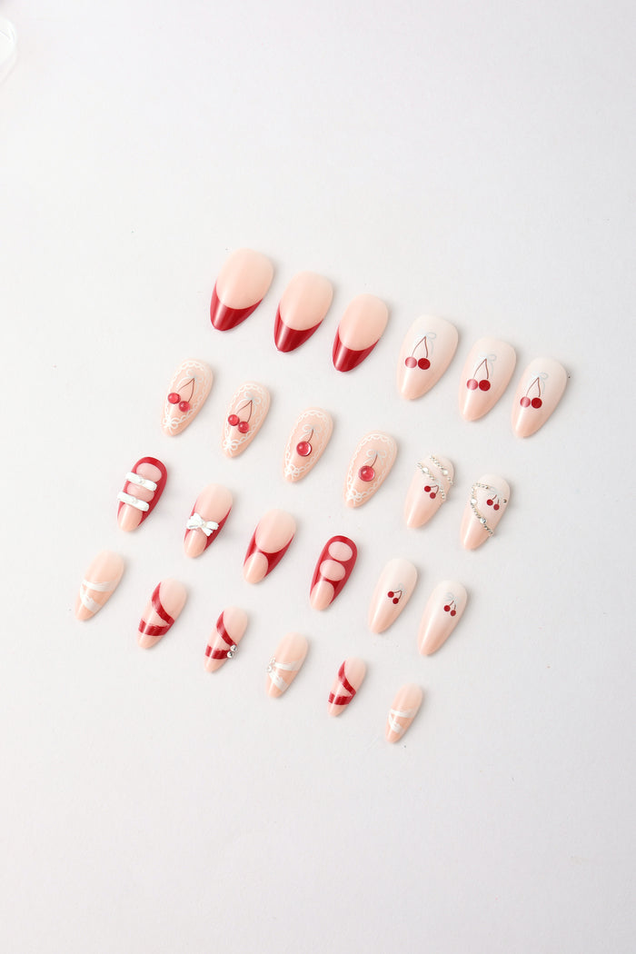 Assorted red and pink press-on nails with cherry, bow, stripe, and rhinestone designs.