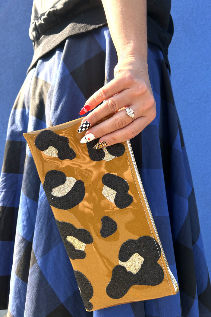 Woman's hand with retro rock 'n' roll press-on nails holding a shiny brown leopard print clutch.