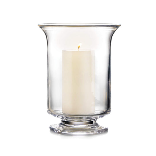 Clear glass hurricane vase with pedestal base holding a lit cream-colored pillar candle.