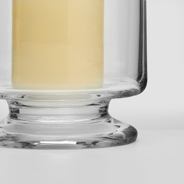Glass hurricane candle holder with cream-colored candle and wide pedestal base.