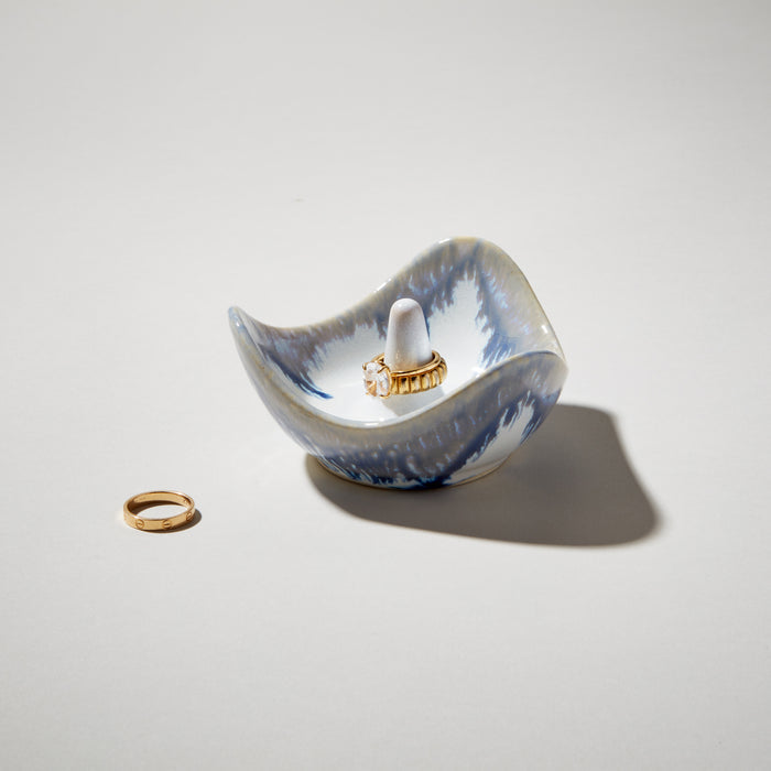 Blue and white ceramic ring holder with small white post, displayed with gold rings.