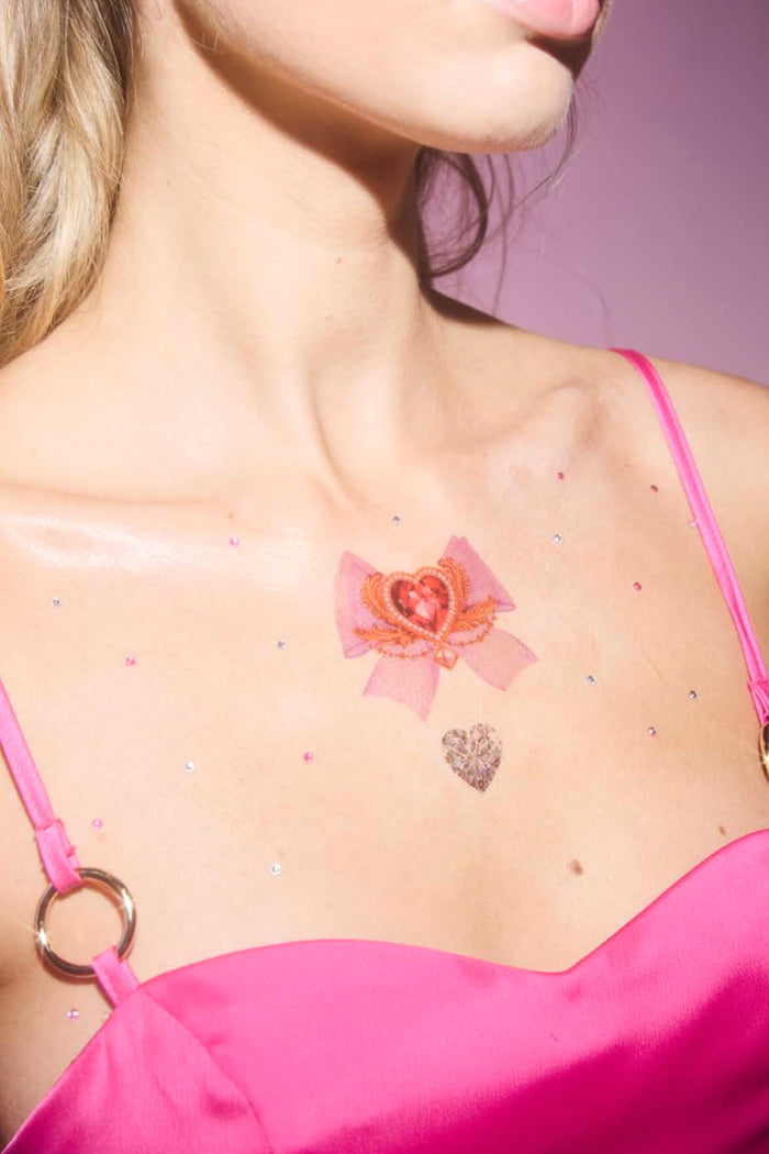 Woman with Rococo Hearts temporary tattoos on her chest, featuring a pink bow with a red gem and a glittery heart.