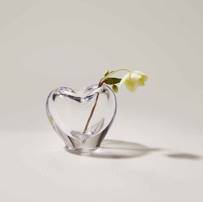 Clear glass heart-shaped vase with yellow flower and brown stem inside.
