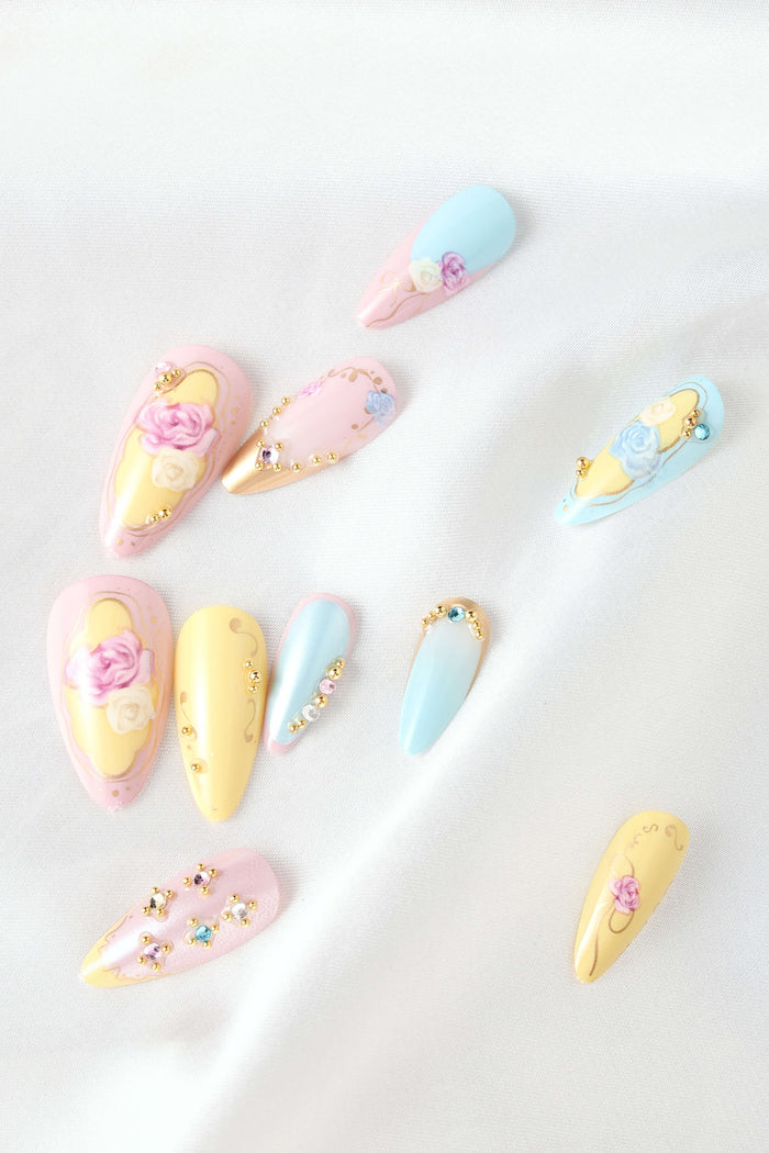 Almond press-on nails with rose garden theme in pastel pink, yellow, and blue with gold accents and gems.