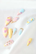 Almond press-on nails with rose garden theme in pastel pink, yellow, and blue with gold accents and gems.
