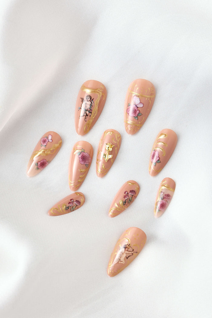 Rose gold almond press-on nails with vintage floral and cupid designs.