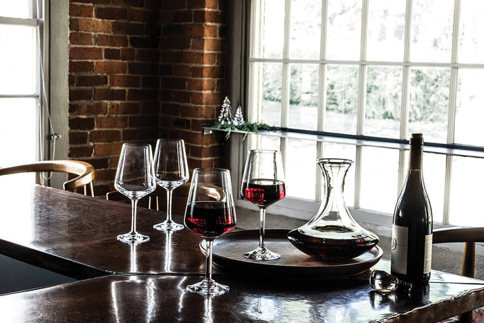 Dark walnut round tray holding wine glasses and a decanter on a dining table.