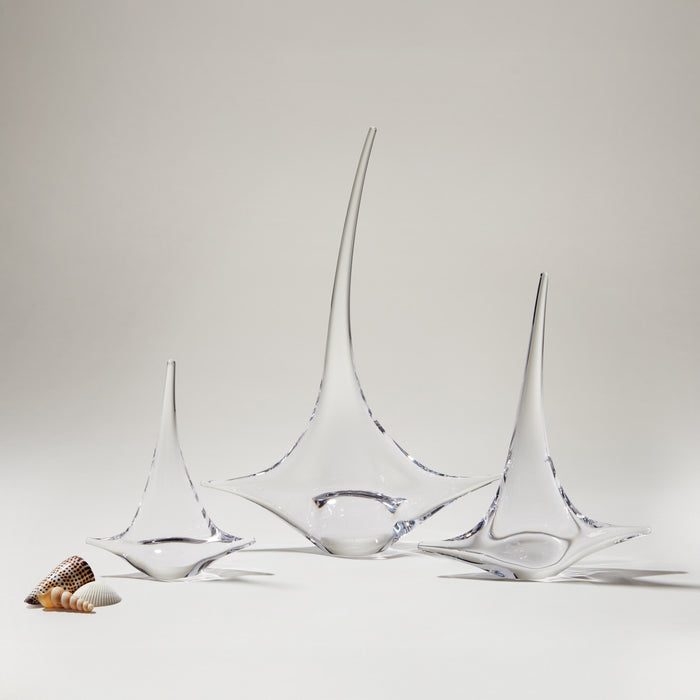Three glass sailboat figurines with blue accents, displayed with small shells on white surface.