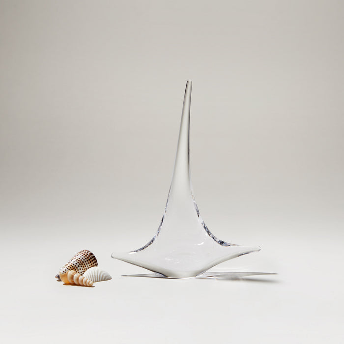 White ceramic sailboat with pointed mast and blue accents, displayed next to small shells on neutral background.