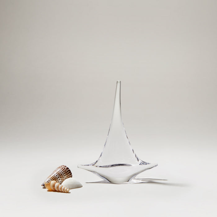 White ceramic sailboat with blue accents next to shells on neutral background.