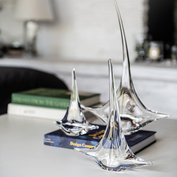 Clear glass sailboat figurines with pointed masts on dark bases, displayed on a desk.