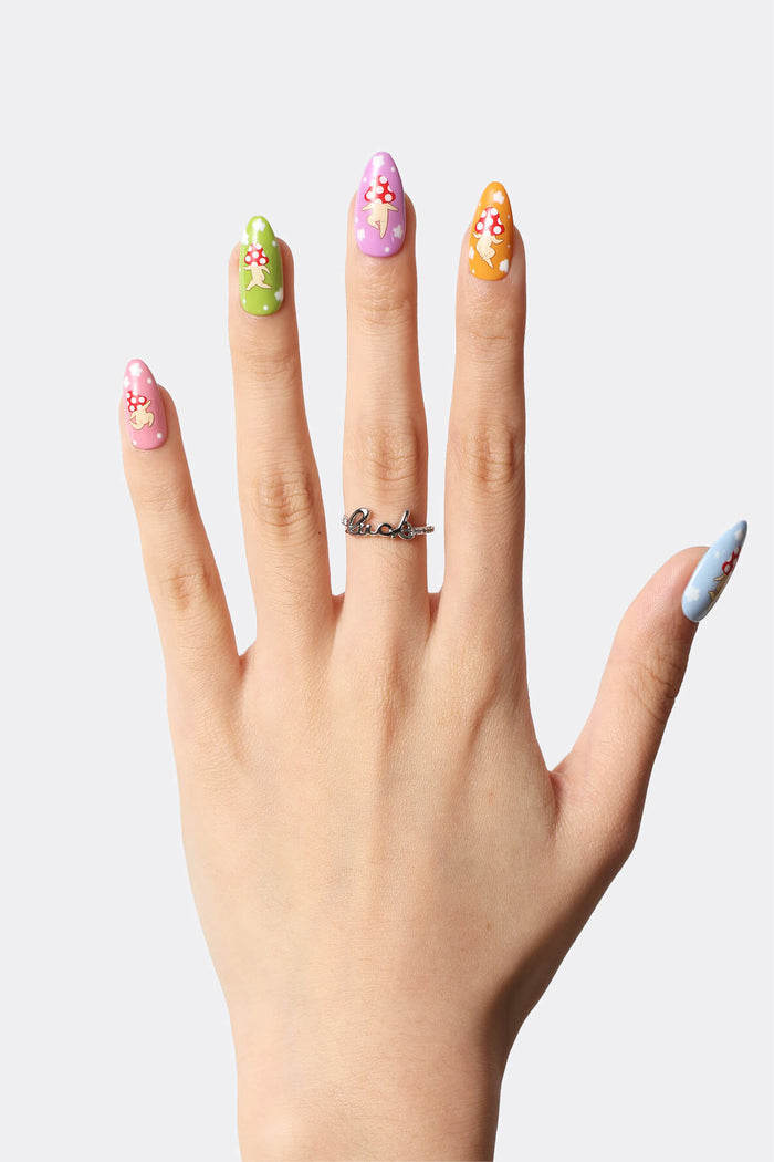Hand with colorful press-on nails featuring mushroom characters and a 'Luck' ring.