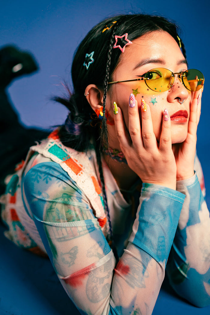 Woman with colorful press-on nails, star hair clips, and yellow sunglasses.