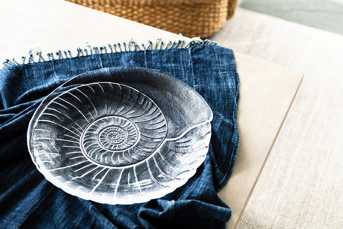 White ceramic platter with spiral shell relief design on blue linen napkin.