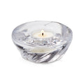 Clear glass shell-shaped tealight holder with lit white candle inside.