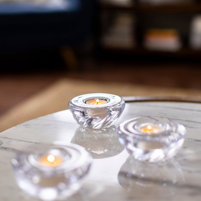 Three clear glass shell-shaped tealight holders with lit candles on a white marble surface.