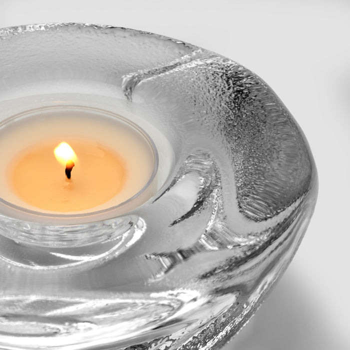 Lit cream tealight inside a silver shell-shaped glass holder with textured surface.