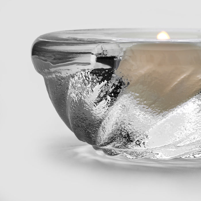 Shell-shaped tealight candle with metallic silver finish and lit flame inside clear glass holder.