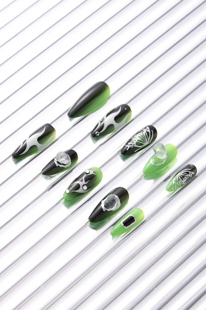 SHE'S A BRAT press-on nails with green and black gradient, flame and butterfly designs, and gem accents.