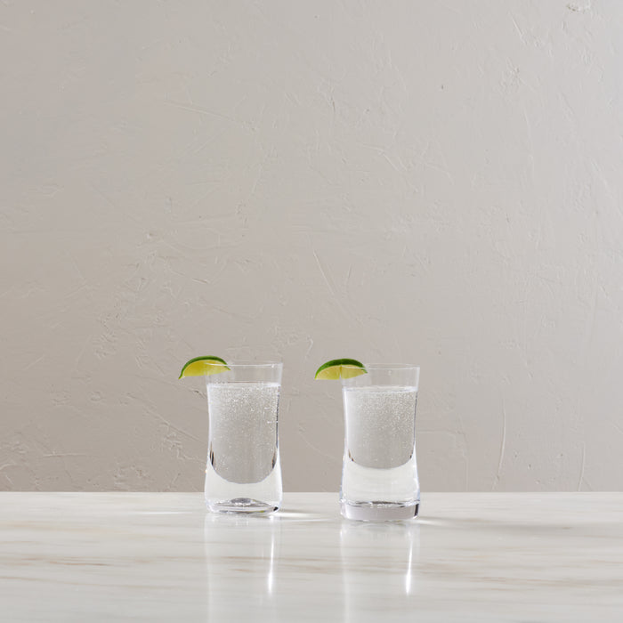 Two clear glasses filled with sparkling water and lime slices on white surface.