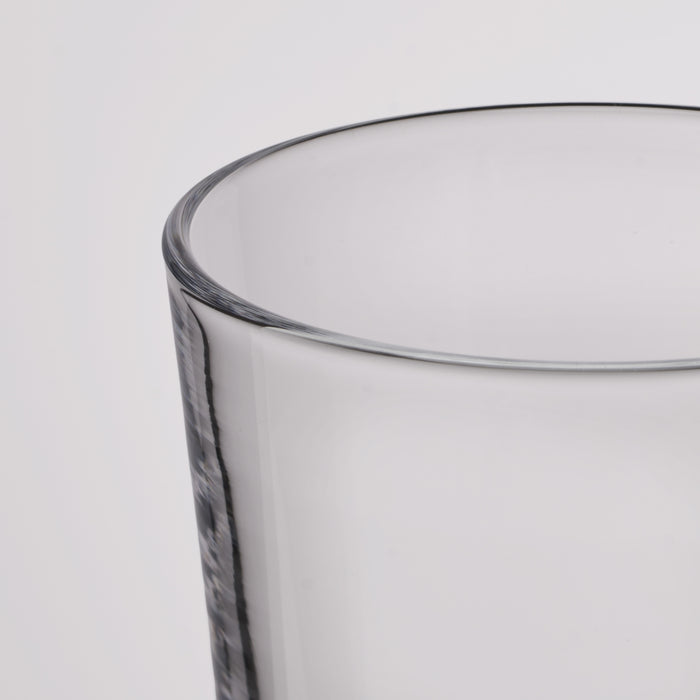 Close-up of a clear glass tumbler showing the rim and part of the textured glass body against a light gray background.