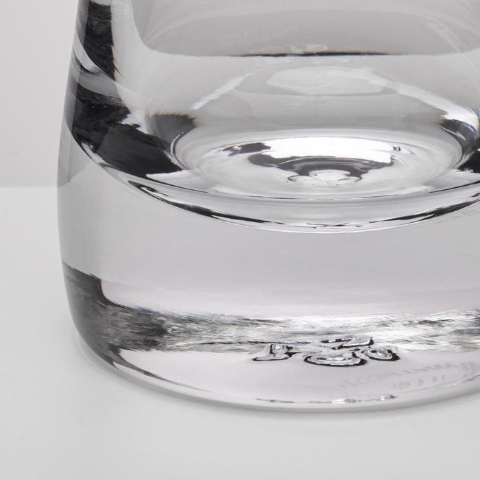 Close-up of a clear glass showing the base and lower body with reflective glass surfaces on a light gray background.