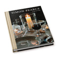 Hardcover book with black dust jacket featuring glassware, a lit candle, and place settings on the cover.