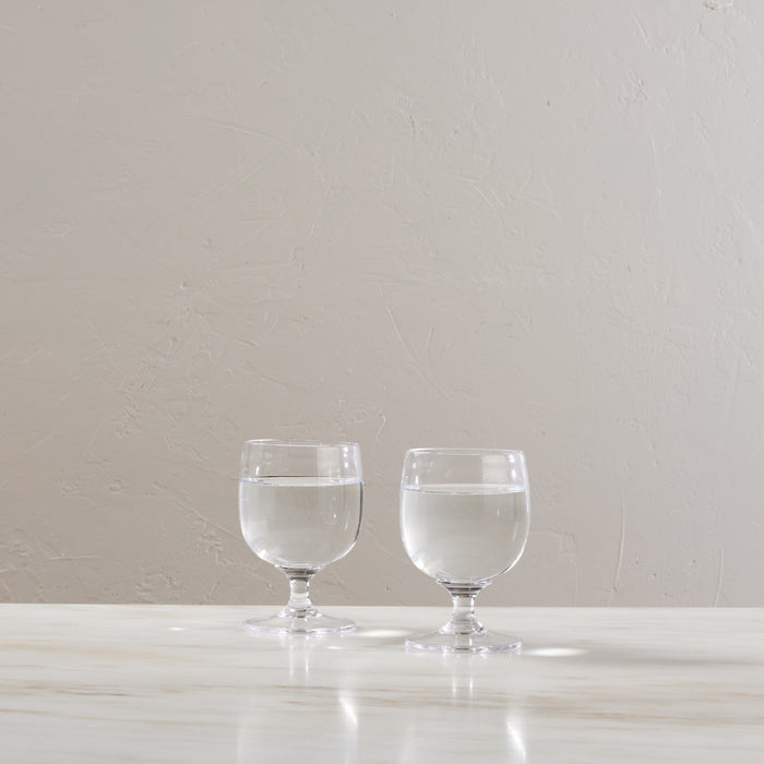 Two clear glass goblets with pedestal bases filled with water, displayed on a white surface.