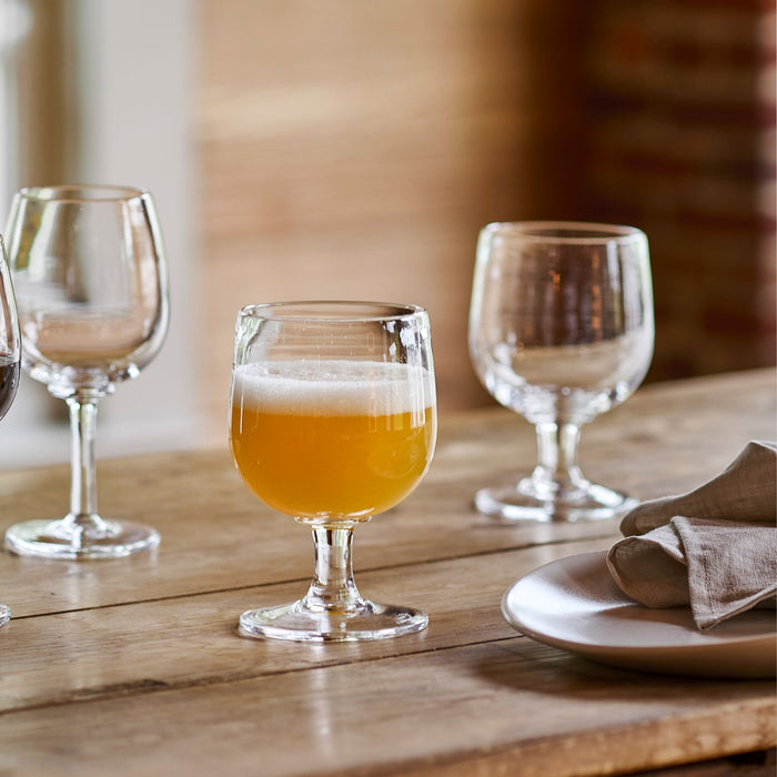 Three clear glass goblets on wooden table, one filled with amber liquid, two empty, with place setting visible.
