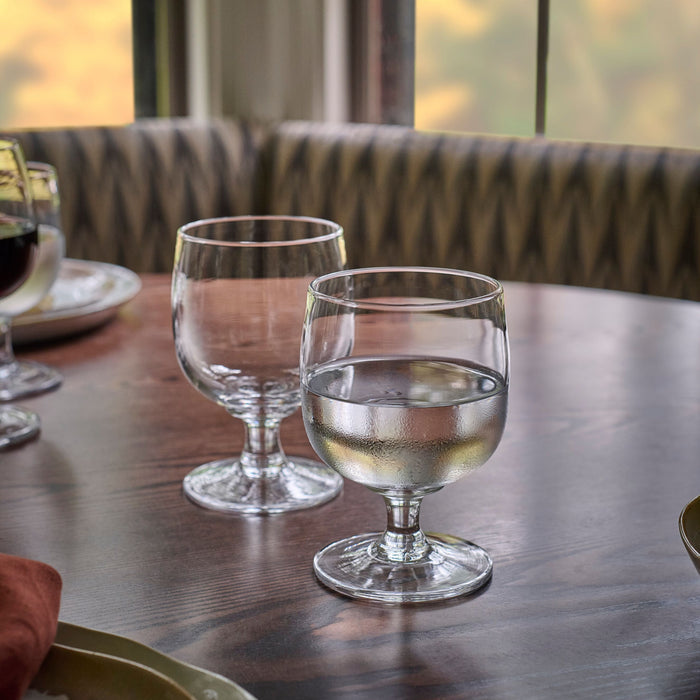 Two clear glass goblets on a dining table, one filled with white wine and one empty.