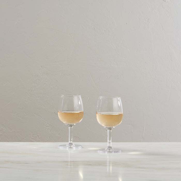 Two clear wine glasses filled with white wine on a white surface against a neutral background.