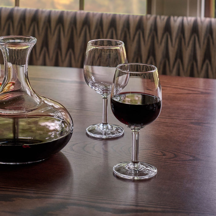 Two clear glass wine glasses, one containing red wine, displayed on a wooden table next to a decanter.
