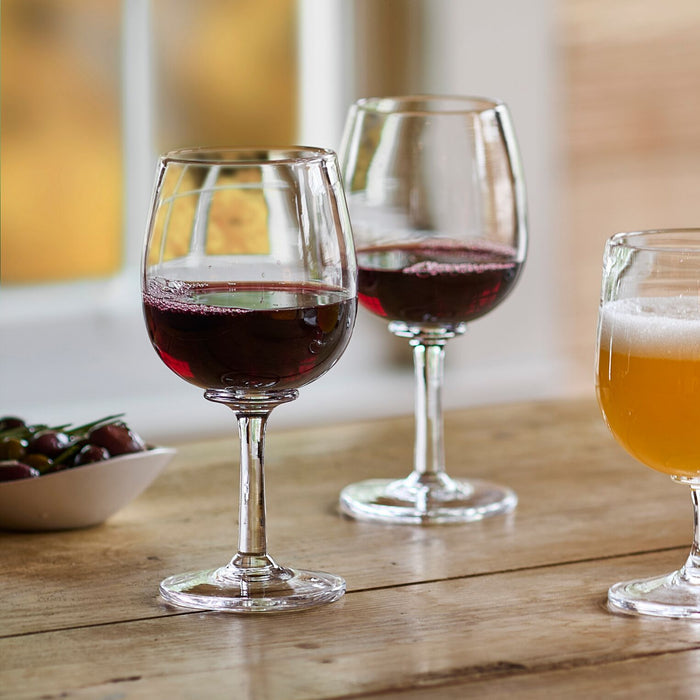 Two clear wine glasses filled with red wine on wooden table with blurred background.