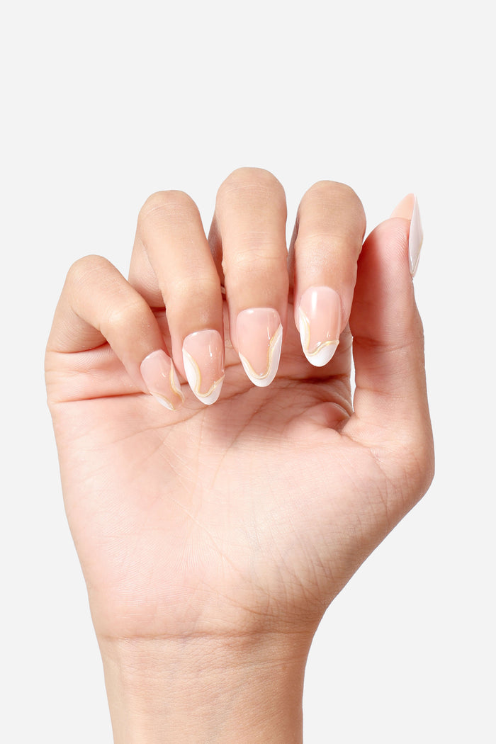 Short almond press-on nails with a nude base, white French tips, and subtle gold wavy accents.